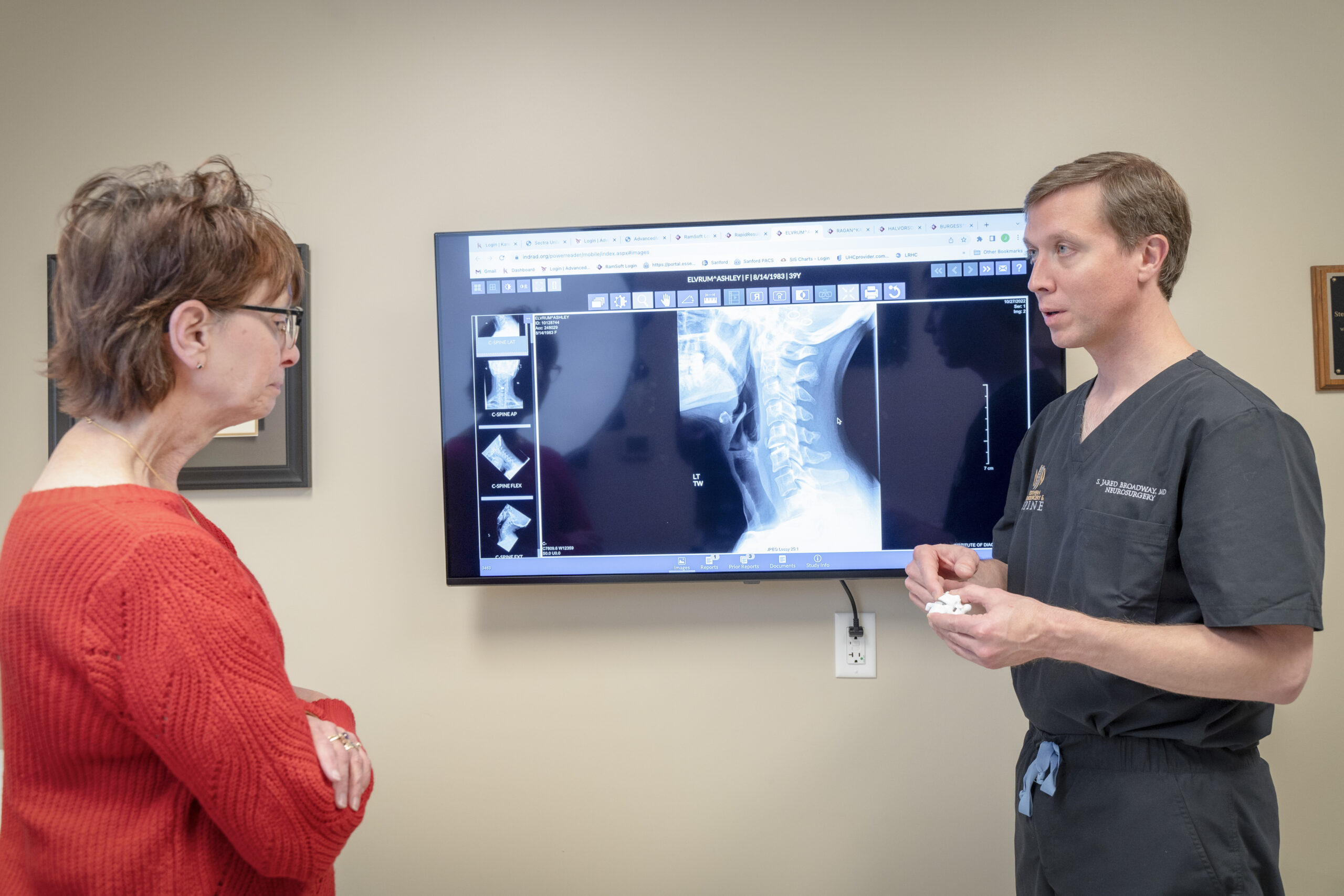 Man in front of xray of the top of a spine, discussing with a woman