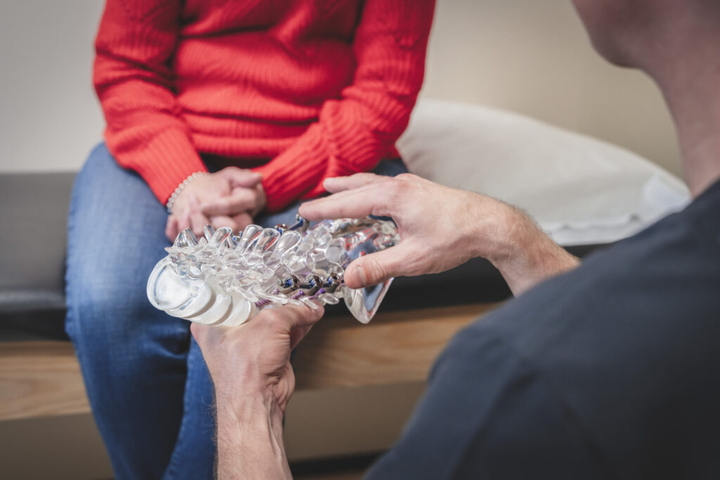 Man with hand over figure of spine with a woman sitting in the background