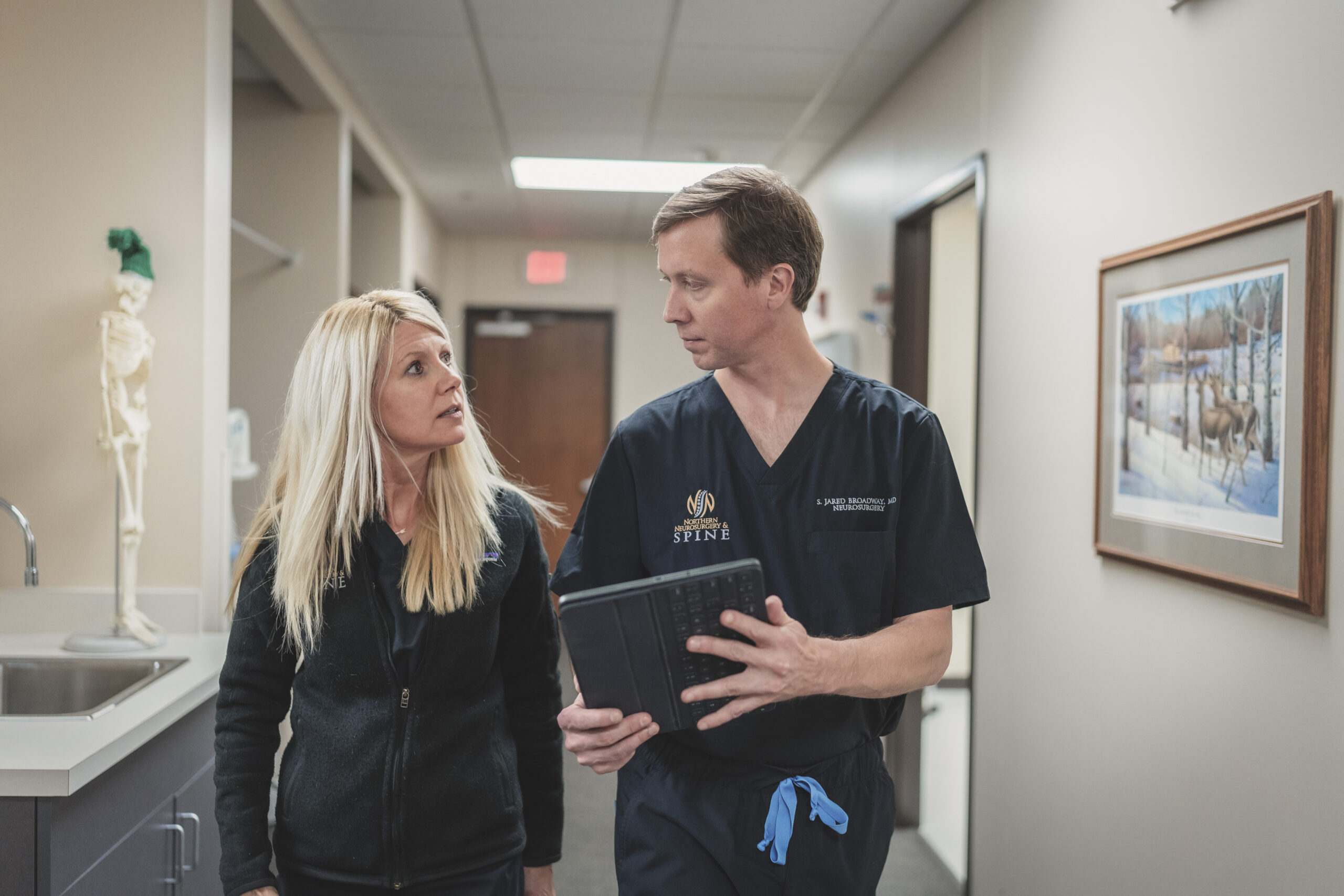 A man and woman in a medical setting discussing something while walking down a hallway.